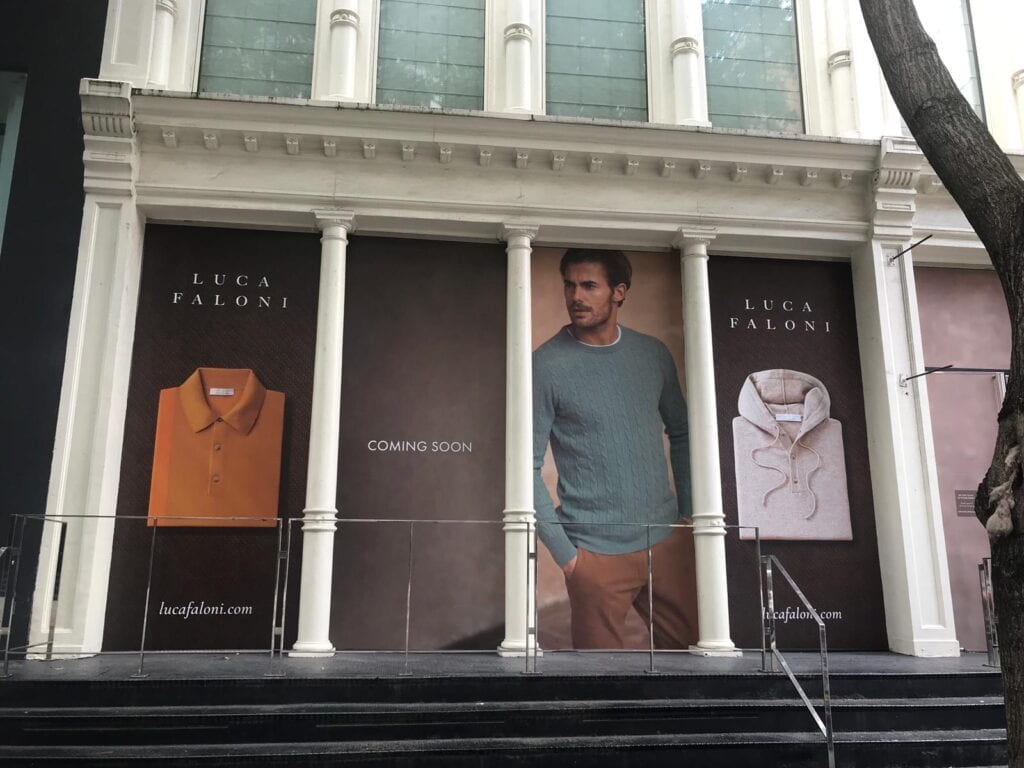 A man standing in front of a building with two large posters.